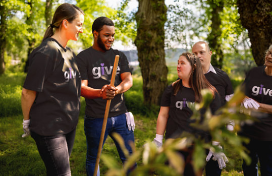 Team of adult volunteers wearing Give mark on their t-shirts helping plant trees and plants.