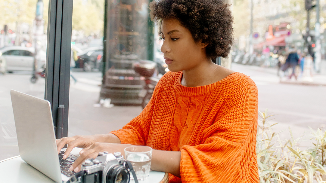 A woman sitting outdoors at a cafe, typing on a laptop