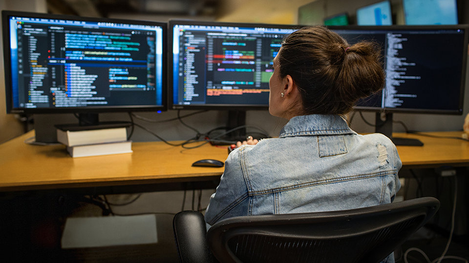 A developer codes on three computer monitors.