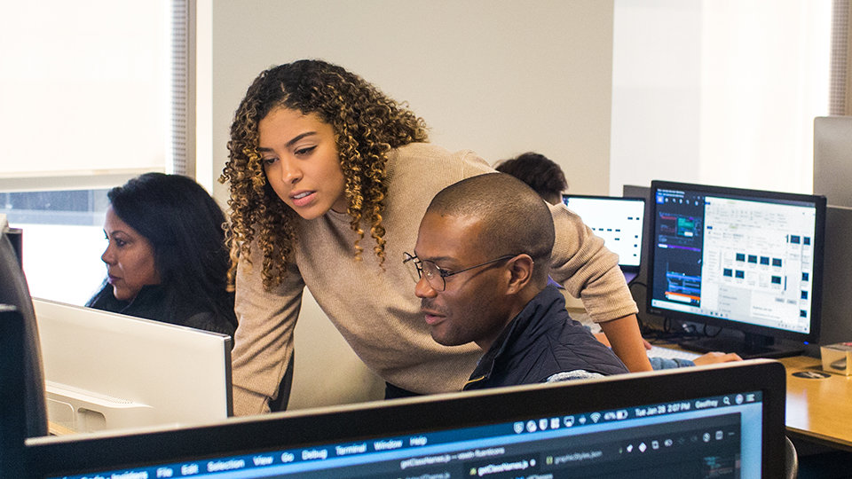 Two coworkers look at a computer monitor together.